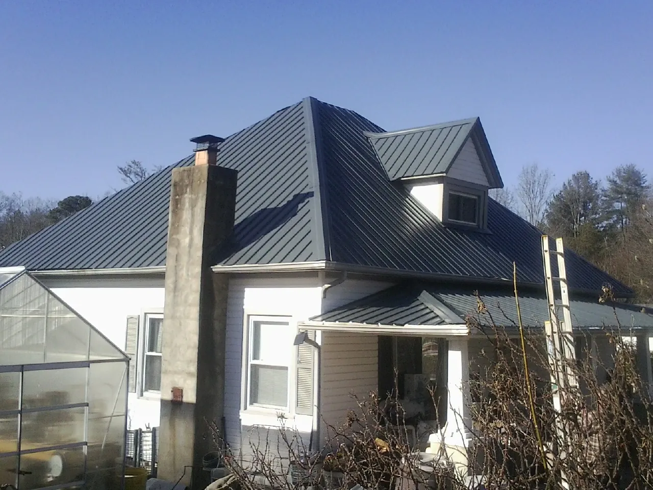 Dark blue standing seam metal roof on a white farmhouse with dormer — Slate & Tile Roof Repair by Roofing Brothers in Buffalo Center