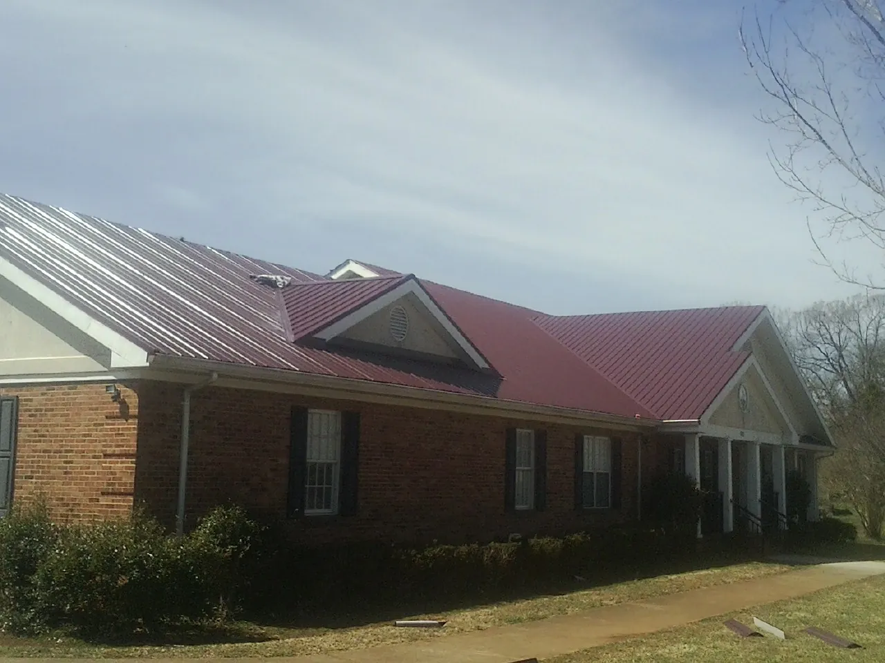 Red metal roof with gabled entries on a long brick building, from a Hail Damage Roof Repair job in Buffalo Center