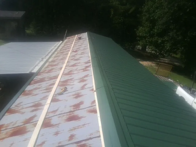 Old rusted panels beside newly installed green metal roofing — Wind Damage Roof Repair by Roofing Brothers in Buffalo Center
