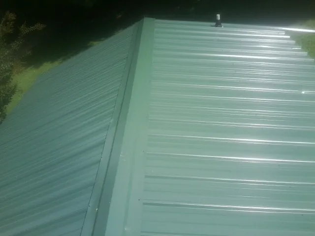 New green metal panels meeting at the ridge of a roof — Flat Roof Repair work by our crew in Buffalo Center