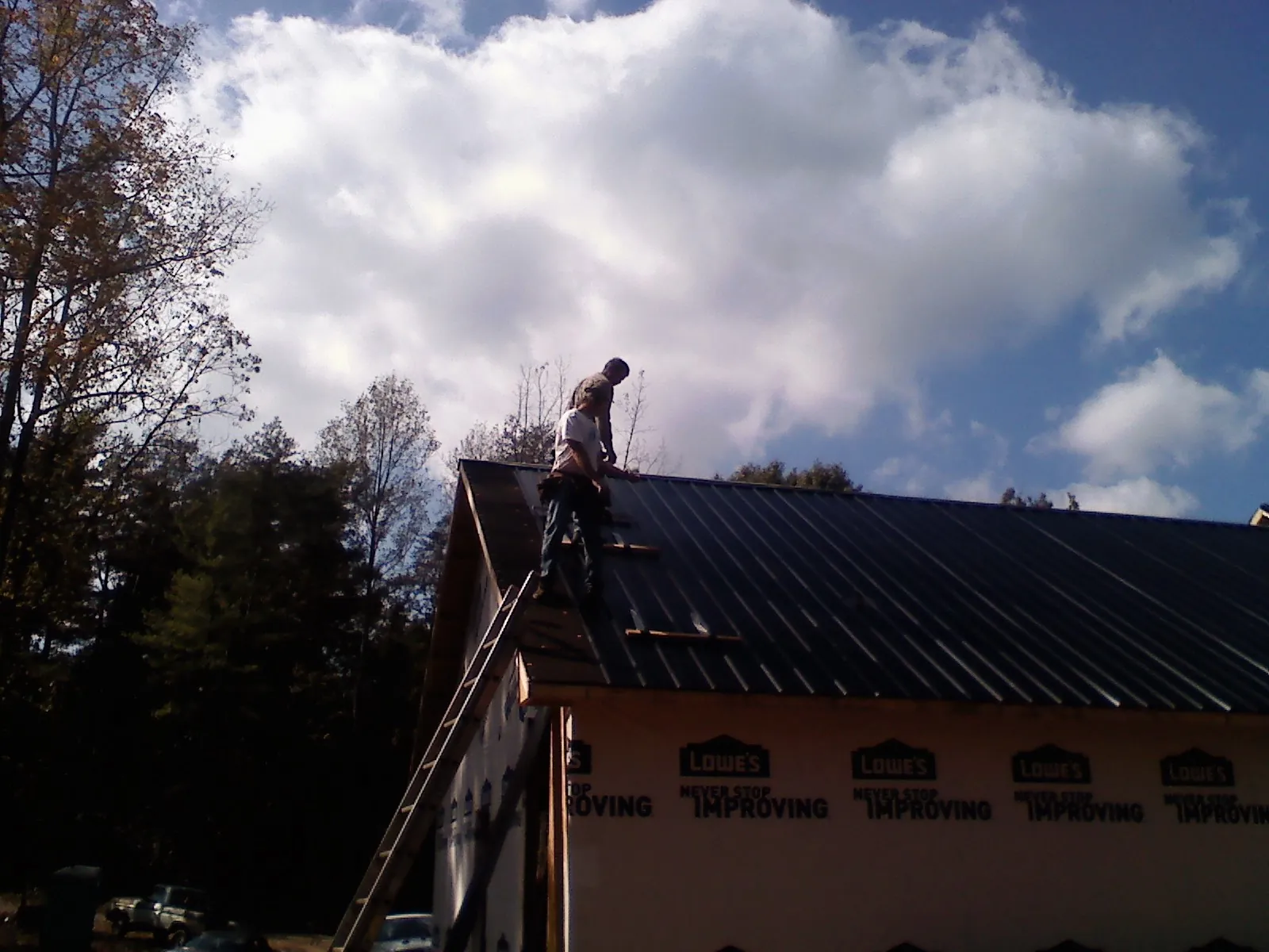 Roofer fastening dark metal panels high against a cloudy sky, from a Roof Inspection job in Buffalo Center
