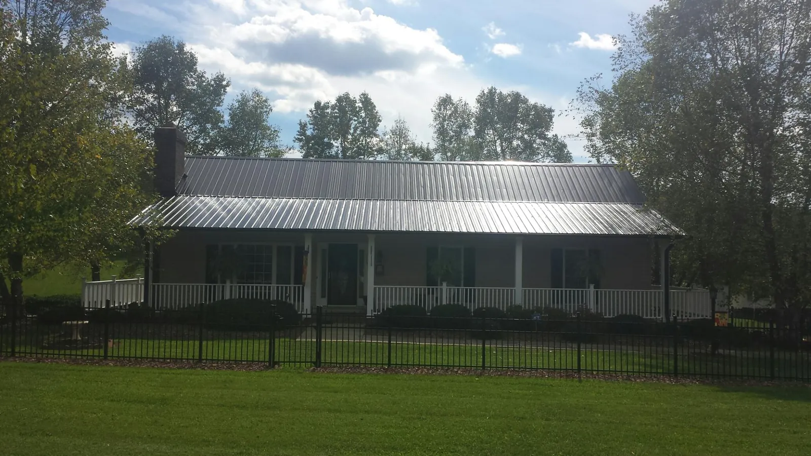Gray metal roof on a brick ranch with a full width front porch — Gutter Guard Installation work by our crew in Buffalo Center