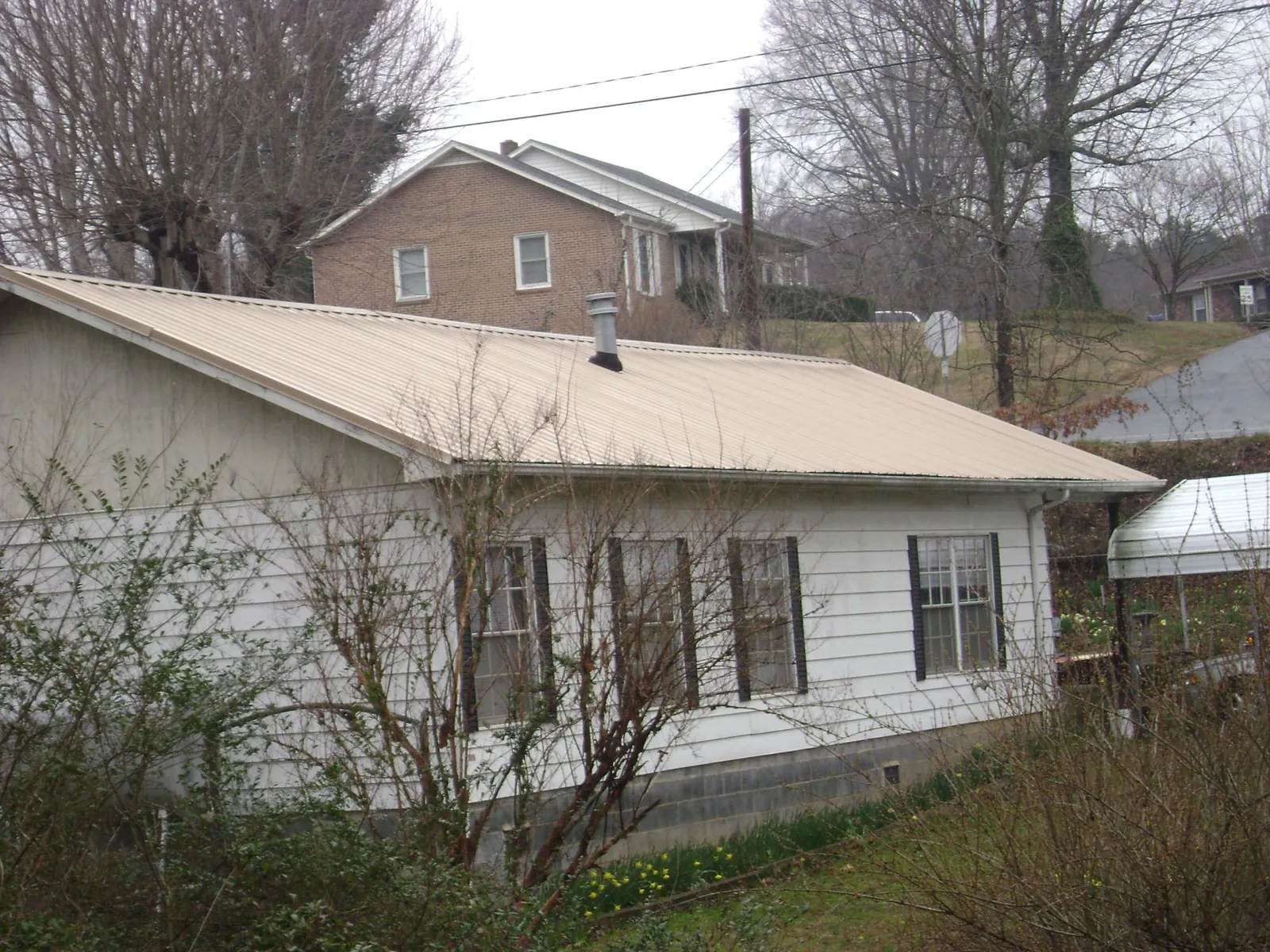 Tan metal roof on a white sided house set into a hillside — Commercial Roofing by Roofing Brothers in Buffalo Center