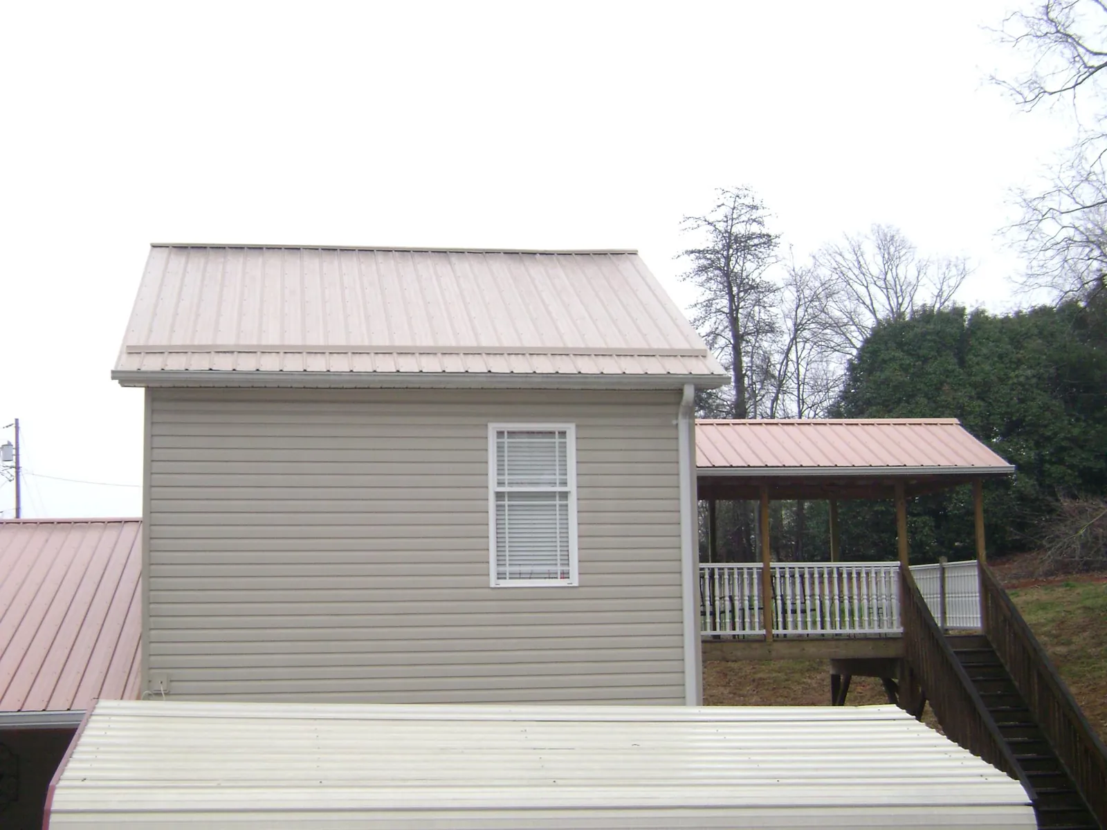 Tan metal roofs on a two story addition and attached porch, from a Roof Replacement job in Buffalo Center